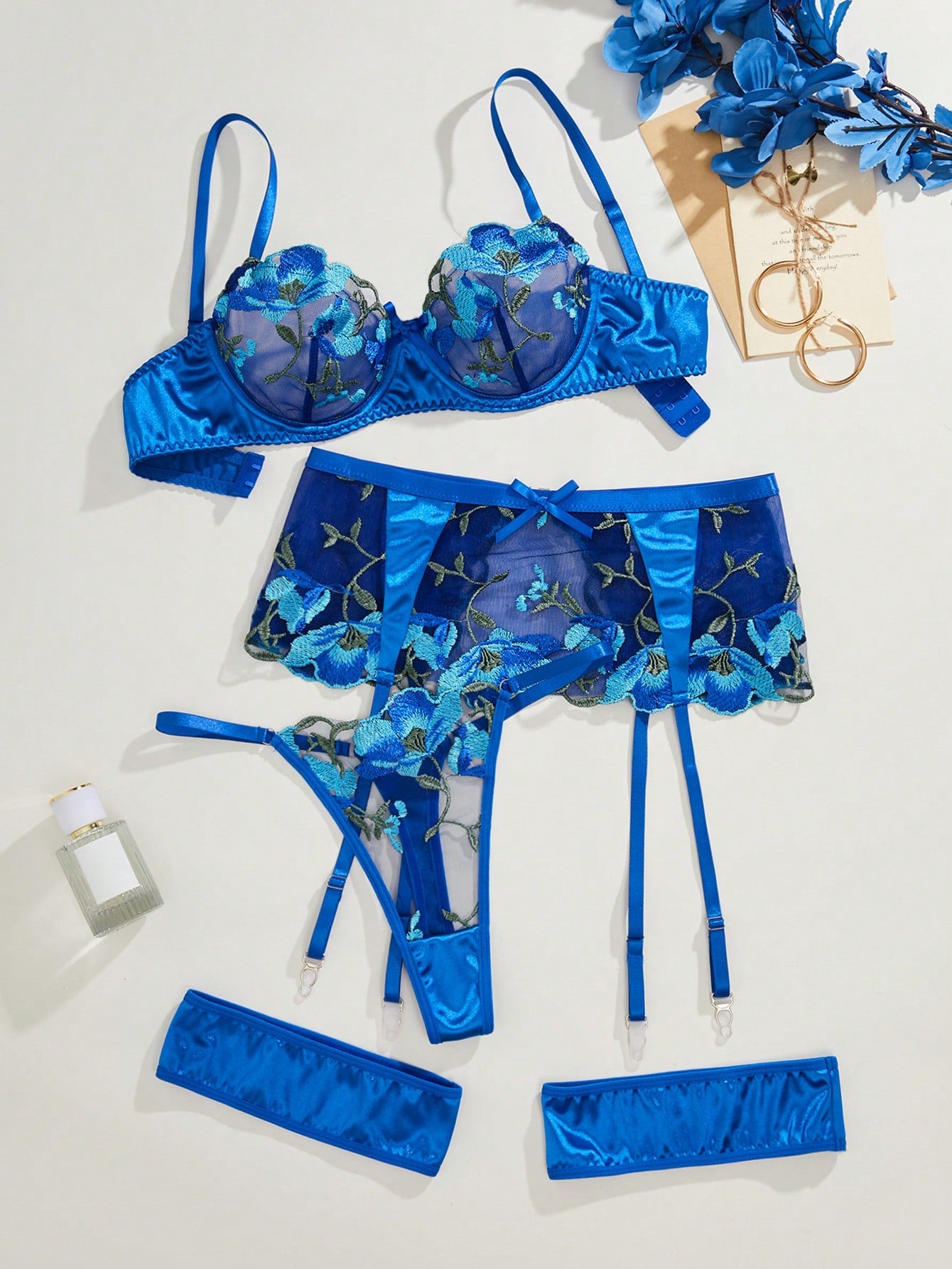 Blue 4-piece lingerie set with floral embroidery and sheer mesh, featuring an underwire demi bra with adjustable spaghetti straps, matching thong, garter details, and one pair of leg rings.