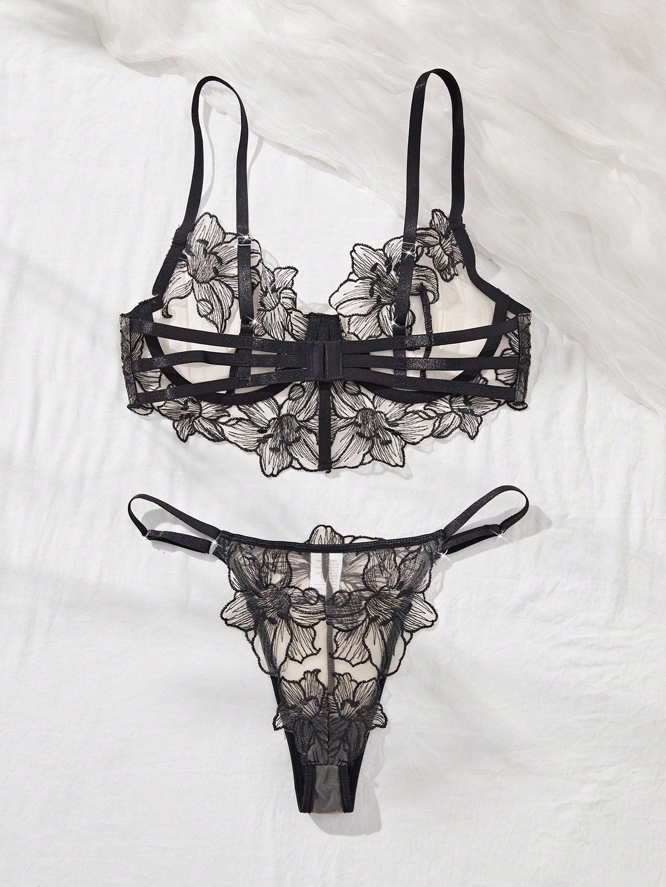Two-piece women’s lingerie set with a sheer balconette underwire bra featuring adjustable straps and matching low-rise thong panty with embroidery and cut-out details.