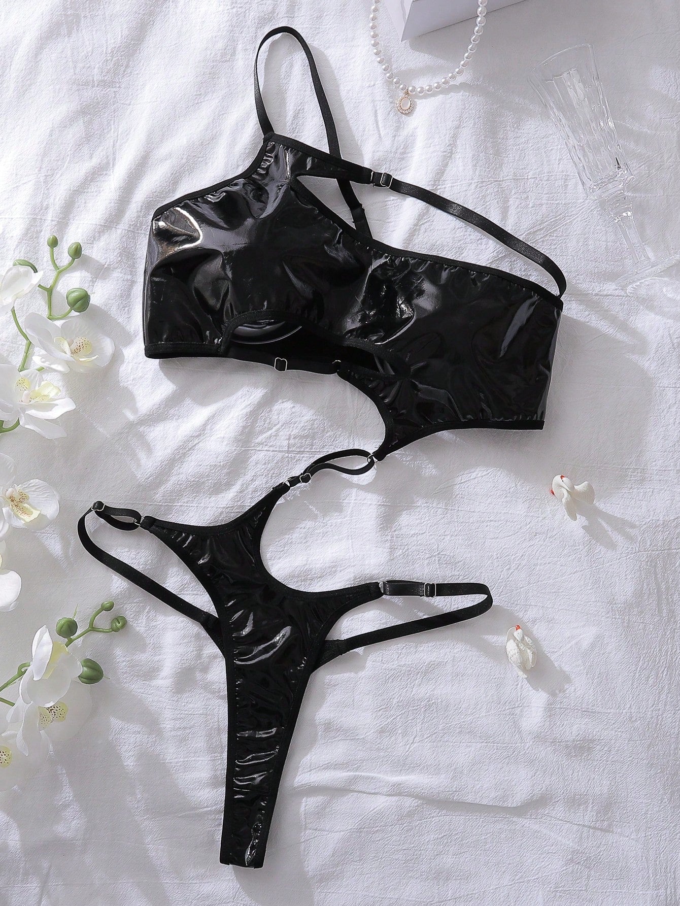 Black women's teddy bodysuit with an asymmetrical neckline, single spaghetti strap, cutout and lace-up line details, sleeveless design, and thong-style bottom.