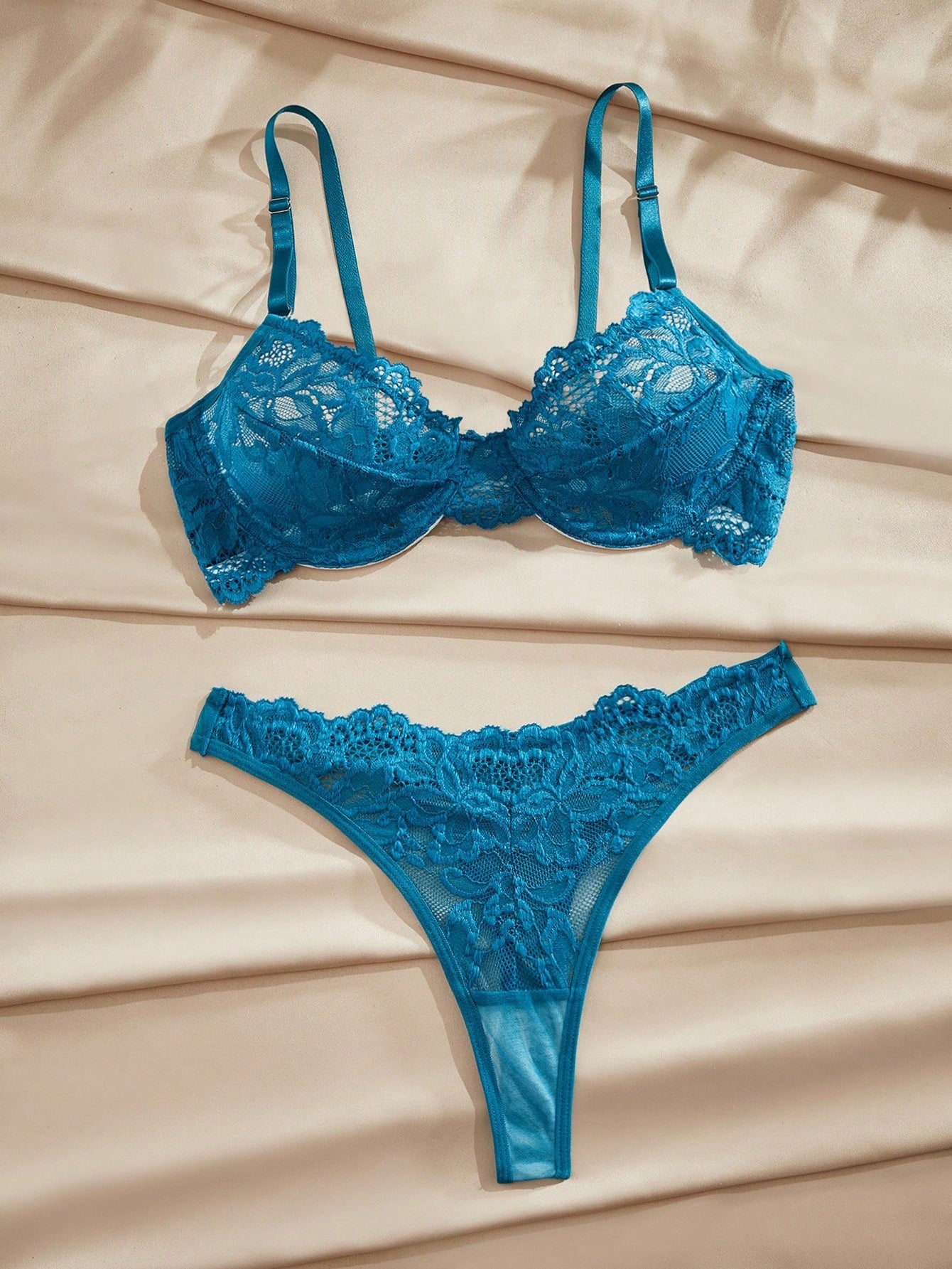 Two-piece teal blue lingerie set with floral lace and sheer fabric, featuring an underwire bra with crossback straps and a matching mid-rise thong.