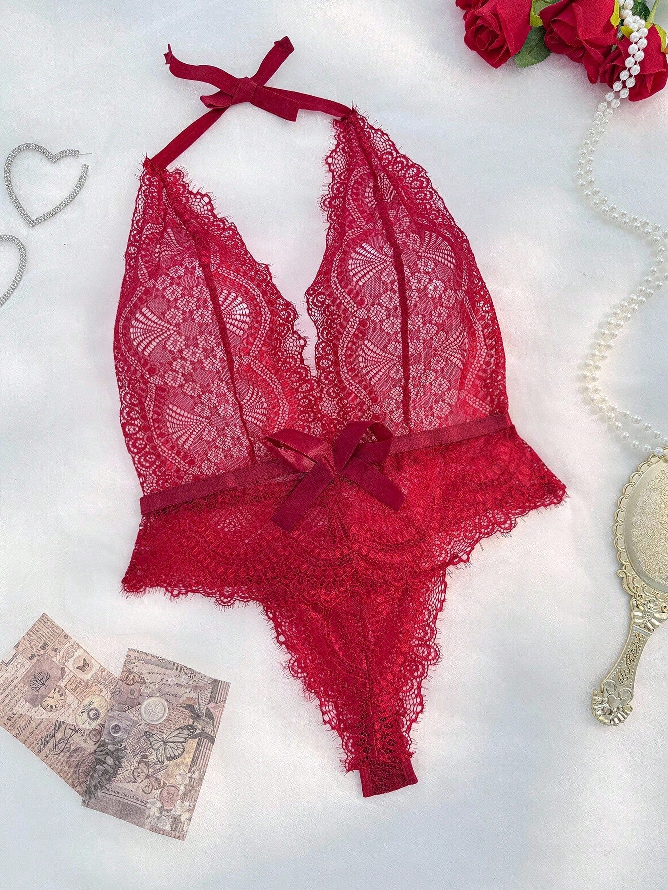 Sheer lace halter bodysuit with a deep V neckline, bow detail, backless cut-out design, and crossback straps.