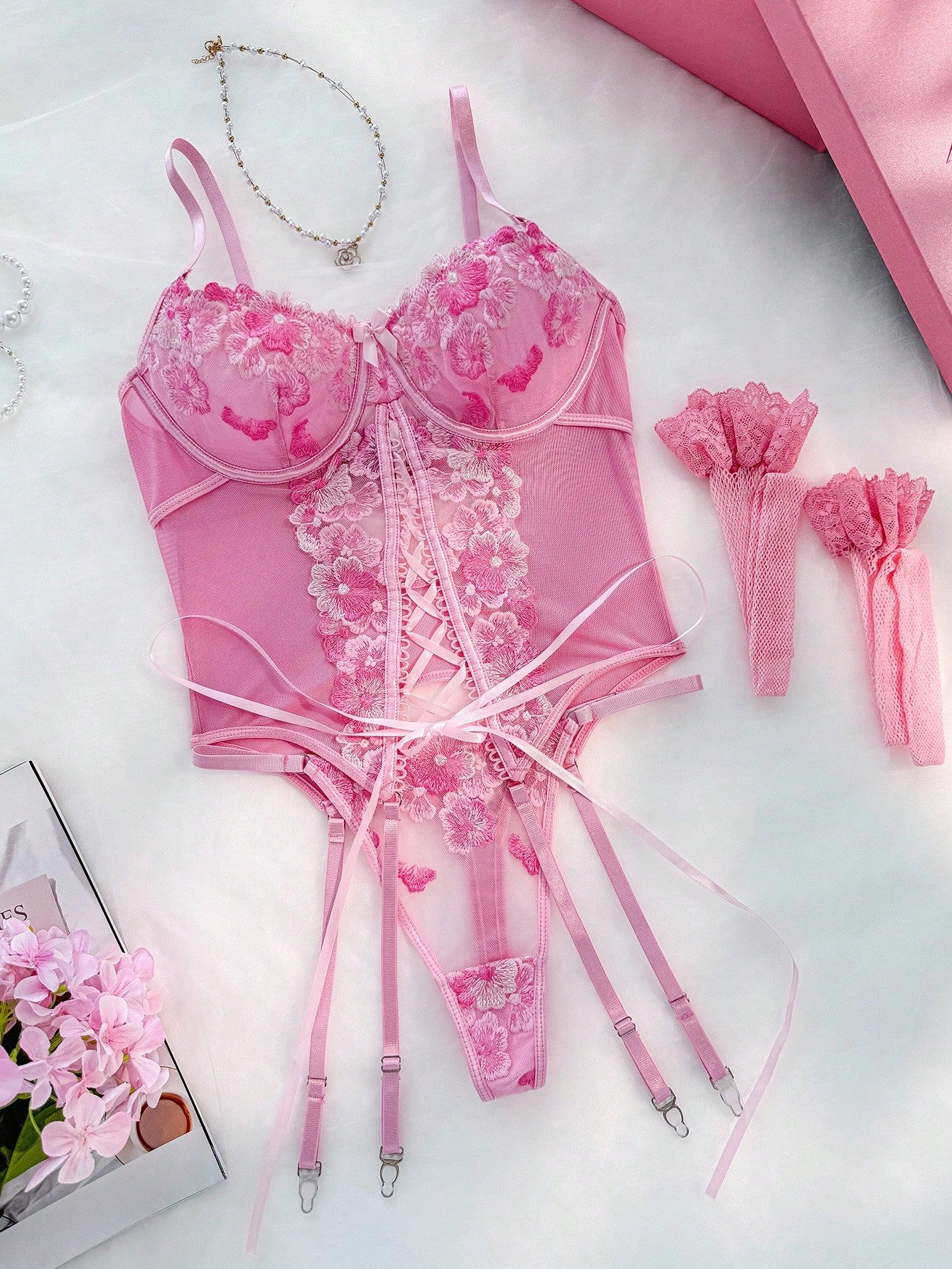 Pink 4-piece women’s lingerie set featuring an underwire bra with contrast mesh and embroidery, a matching G-string thong, and two fishnet stockings; adjustable spaghetti straps and lace-up detail.