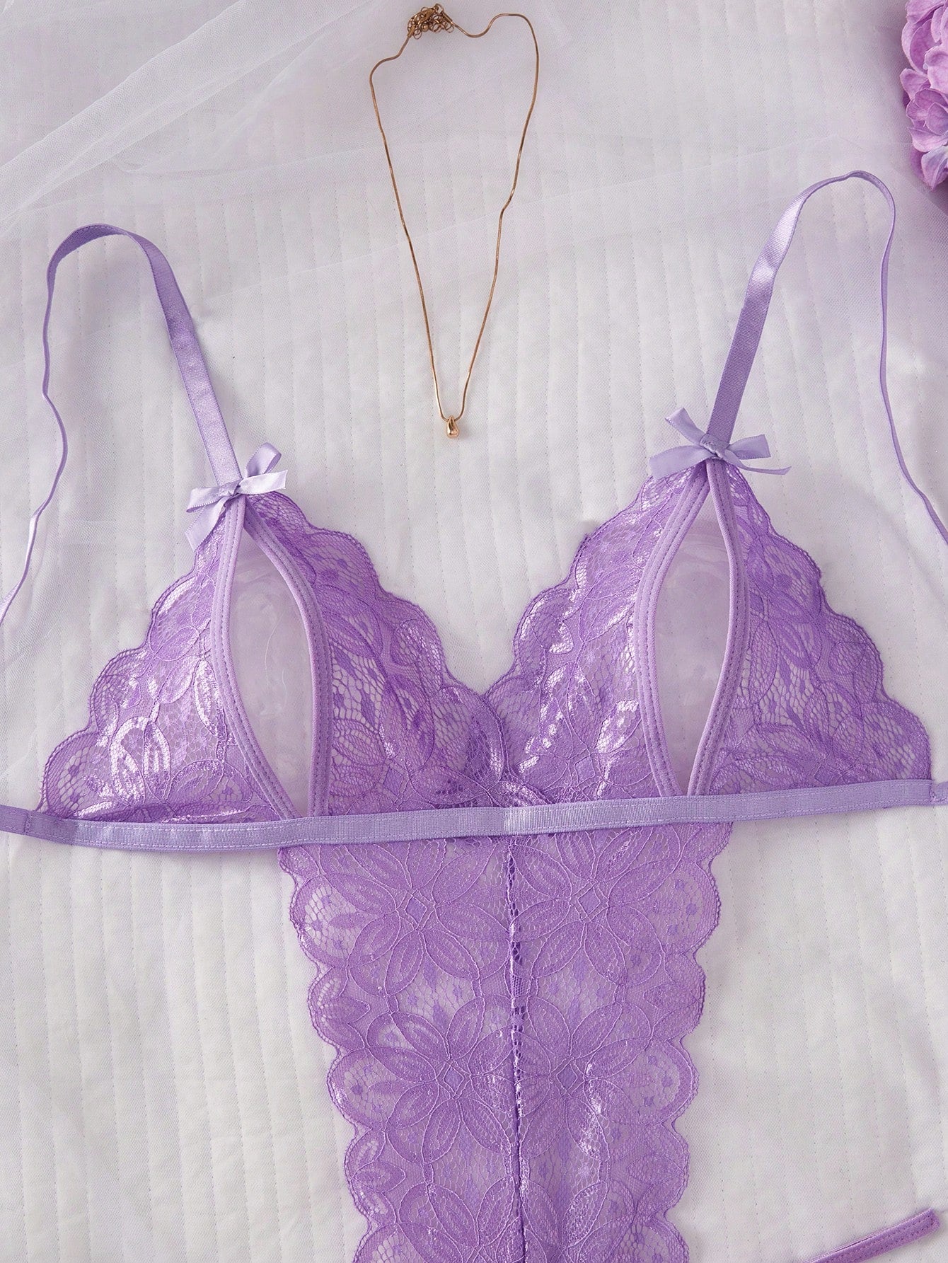 Purple women's sexy lingerie bodysuit with deep V-neck, sheer contrast floral lace, hollow-out details, bow decor, adjustable spaghetti straps, backless design, and crotchless thong-style bottom.