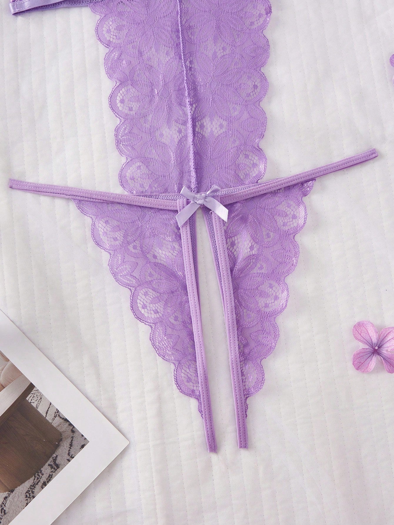 Purple women's sexy lingerie bodysuit with deep V-neck, sheer contrast floral lace, hollow-out details, bow decor, adjustable spaghetti straps, backless design, and crotchless thong-style bottom.