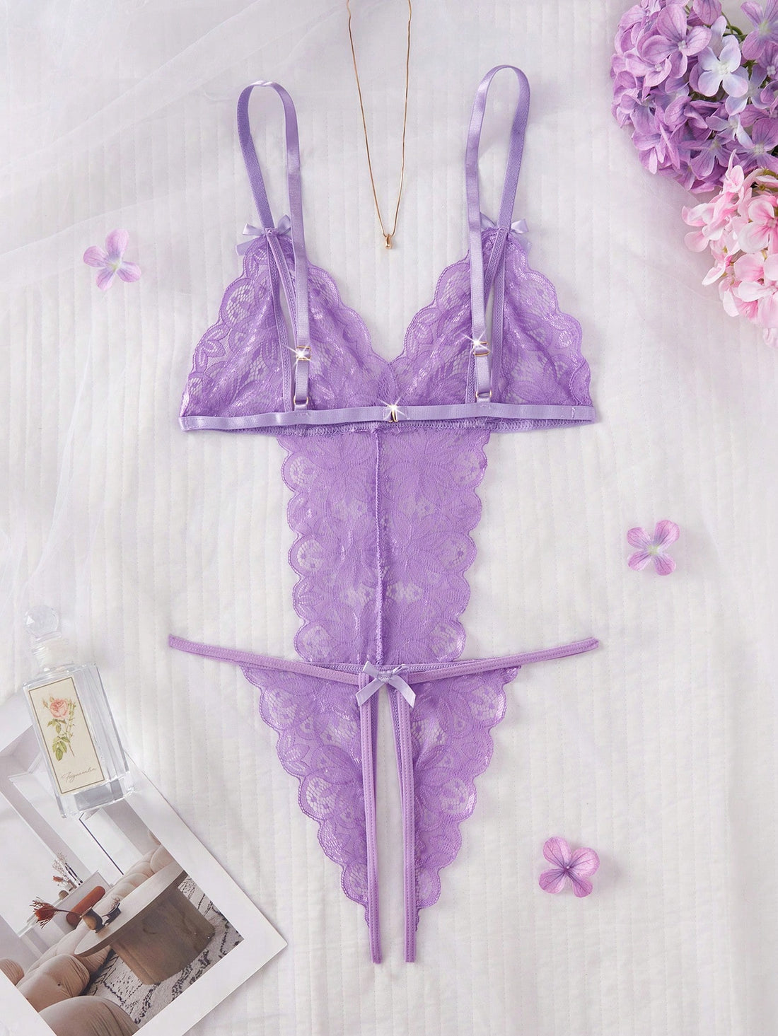 Purple women's sexy lingerie bodysuit with deep V-neck, sheer contrast floral lace, hollow-out details, bow decor, adjustable spaghetti straps, backless design, and crotchless thong-style bottom.
