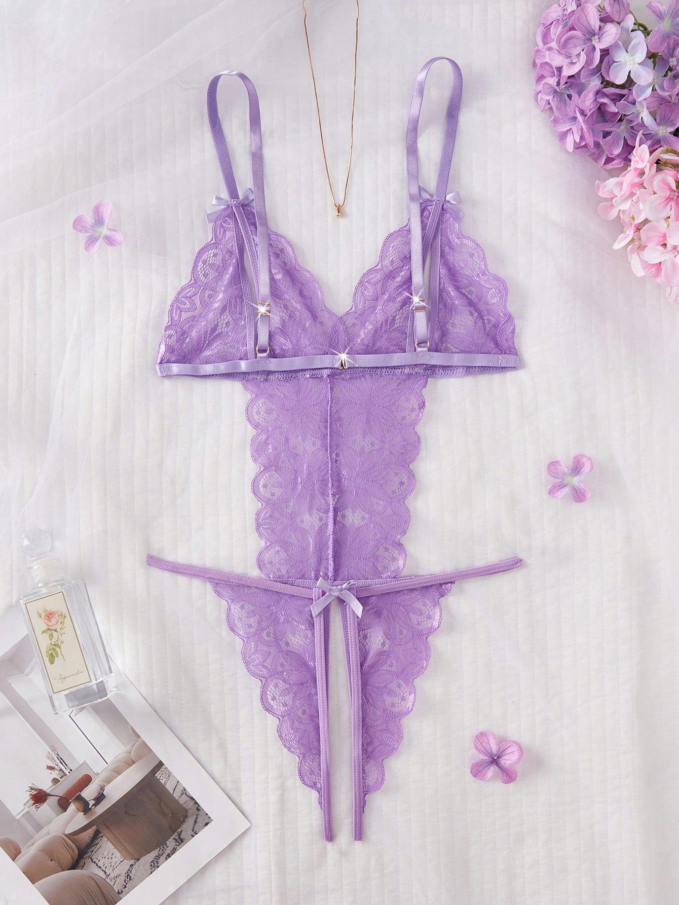 Purple women's sexy lingerie bodysuit with deep V-neck, sheer contrast floral lace, hollow-out details, bow decor, adjustable spaghetti straps, backless design, and crotchless thong-style bottom.