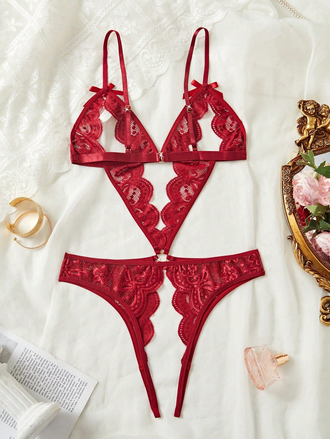 Women's burgundy teddy lingerie bodysuit featuring adjustable spaghetti straps, bow decor, exposed chest design, scalloped trim, metal heart detail, backless semi-sheer contrast lace, and thong-style low-rise bottom.
