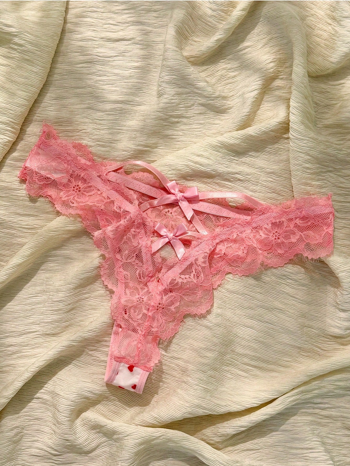 Women's pink heart flocked thong panties with sheer detailing, lace trim, geometric pattern accents, and a mid-rise romantic-floral style.