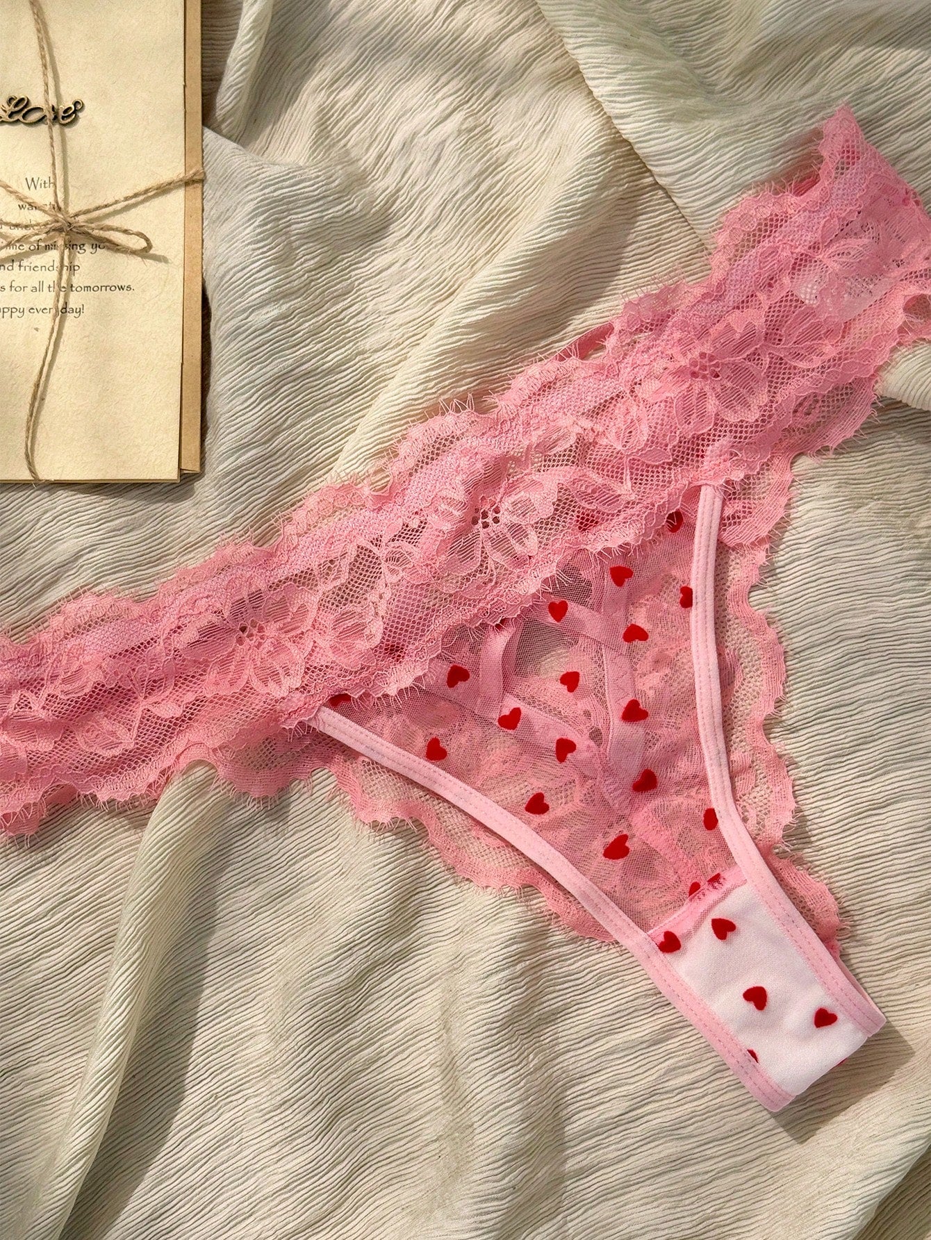 Women's pink heart flocked thong panties with sheer detailing, lace trim, geometric pattern accents, and a mid-rise romantic-floral style.