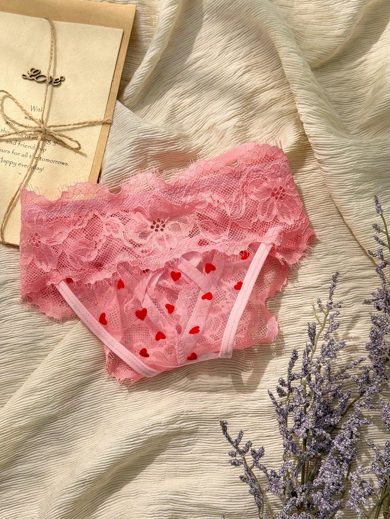 Women's pink heart flocked thong panties with sheer detailing, lace trim, geometric pattern accents, and a mid-rise romantic-floral style.