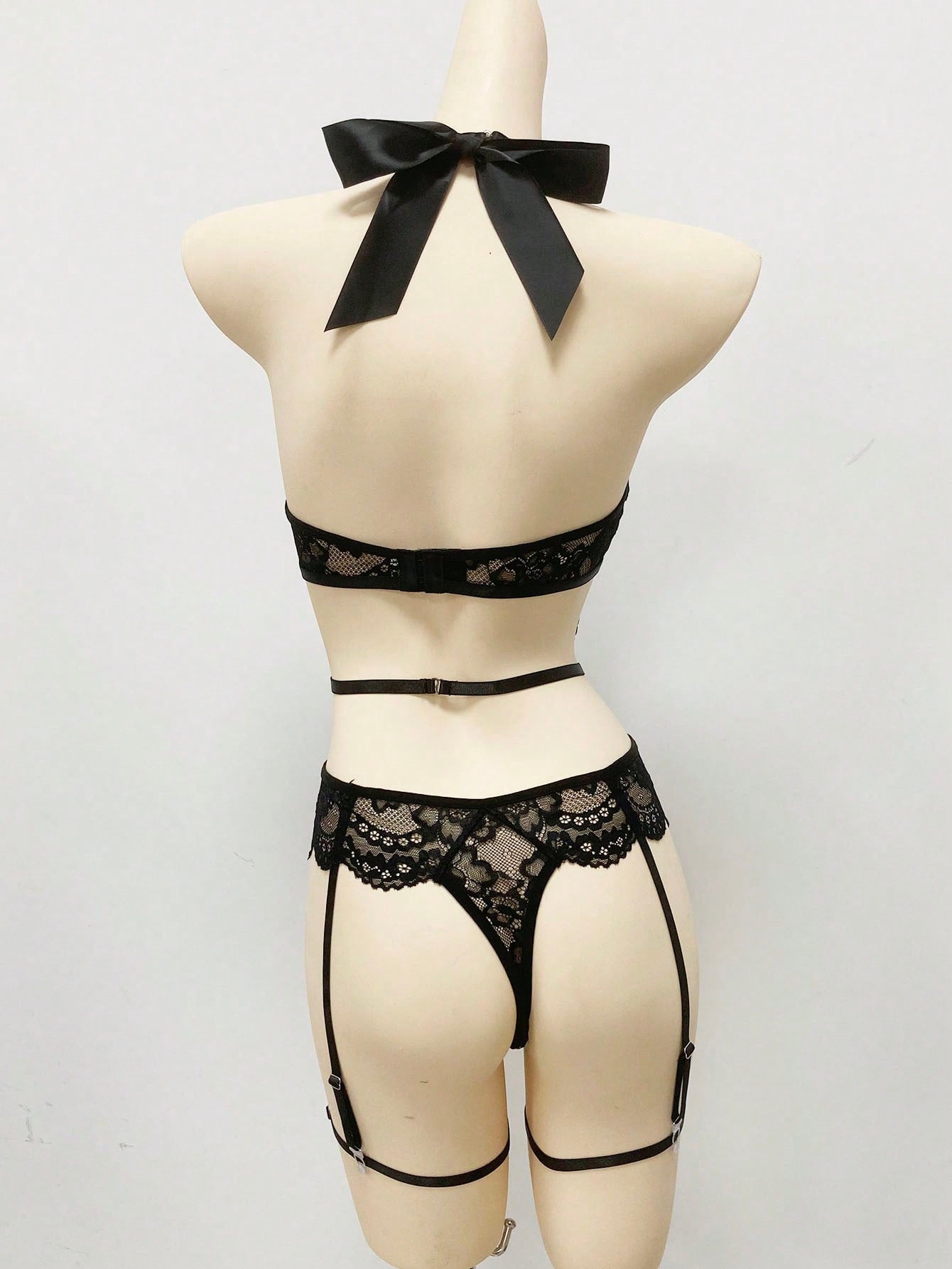 Black women's lace bowknot decorated lingerie set featuring a sleeveless spaghetti strap bodysuit with underwire, cut-out and scallop details, plus matching low-rise thong pieces in a 3-piece set.