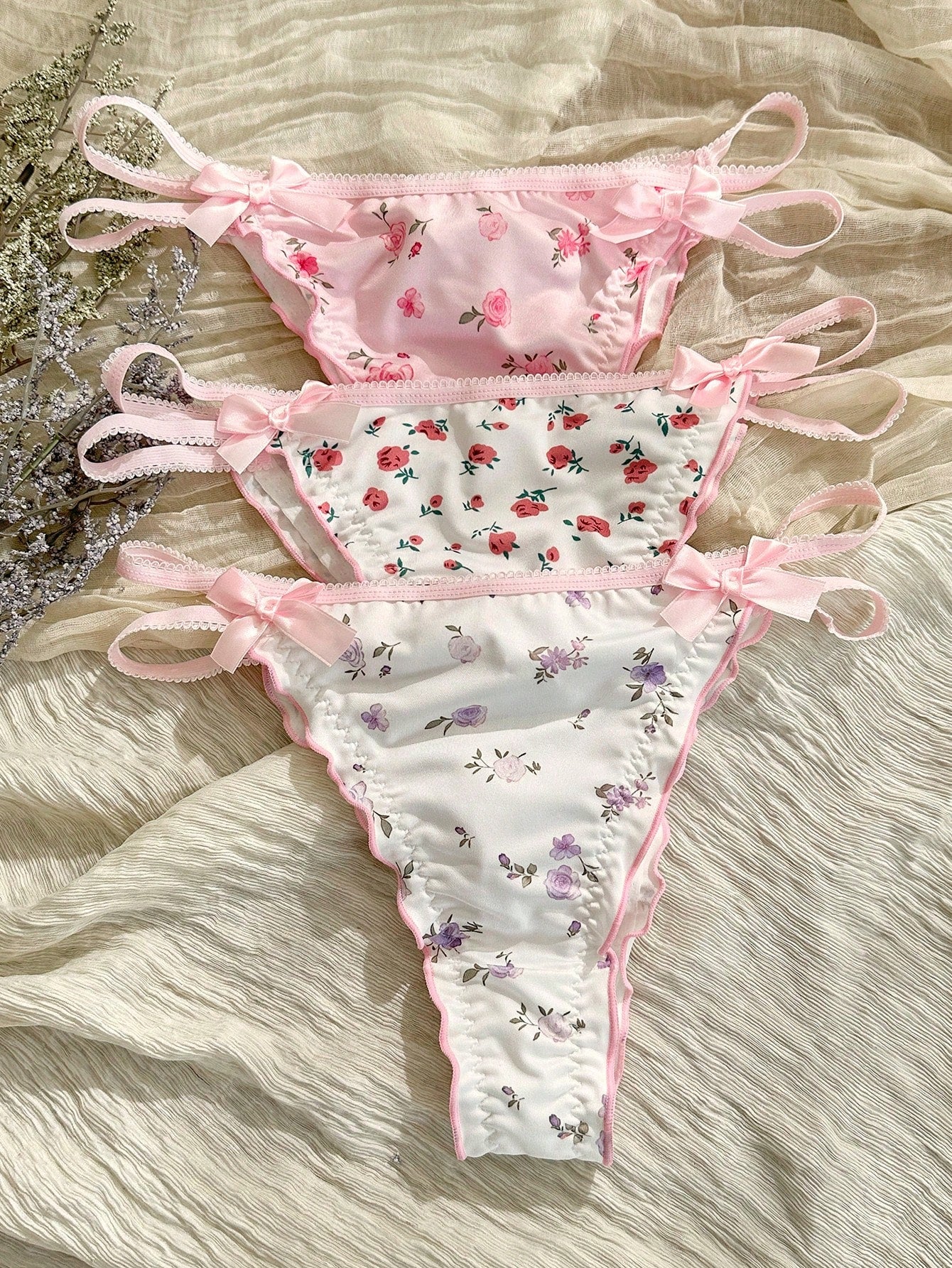 Three-piece set of pink women's low-rise brief panties with floral styling, bow waist accents, contrast lace, contrast binding, and cut-out details.