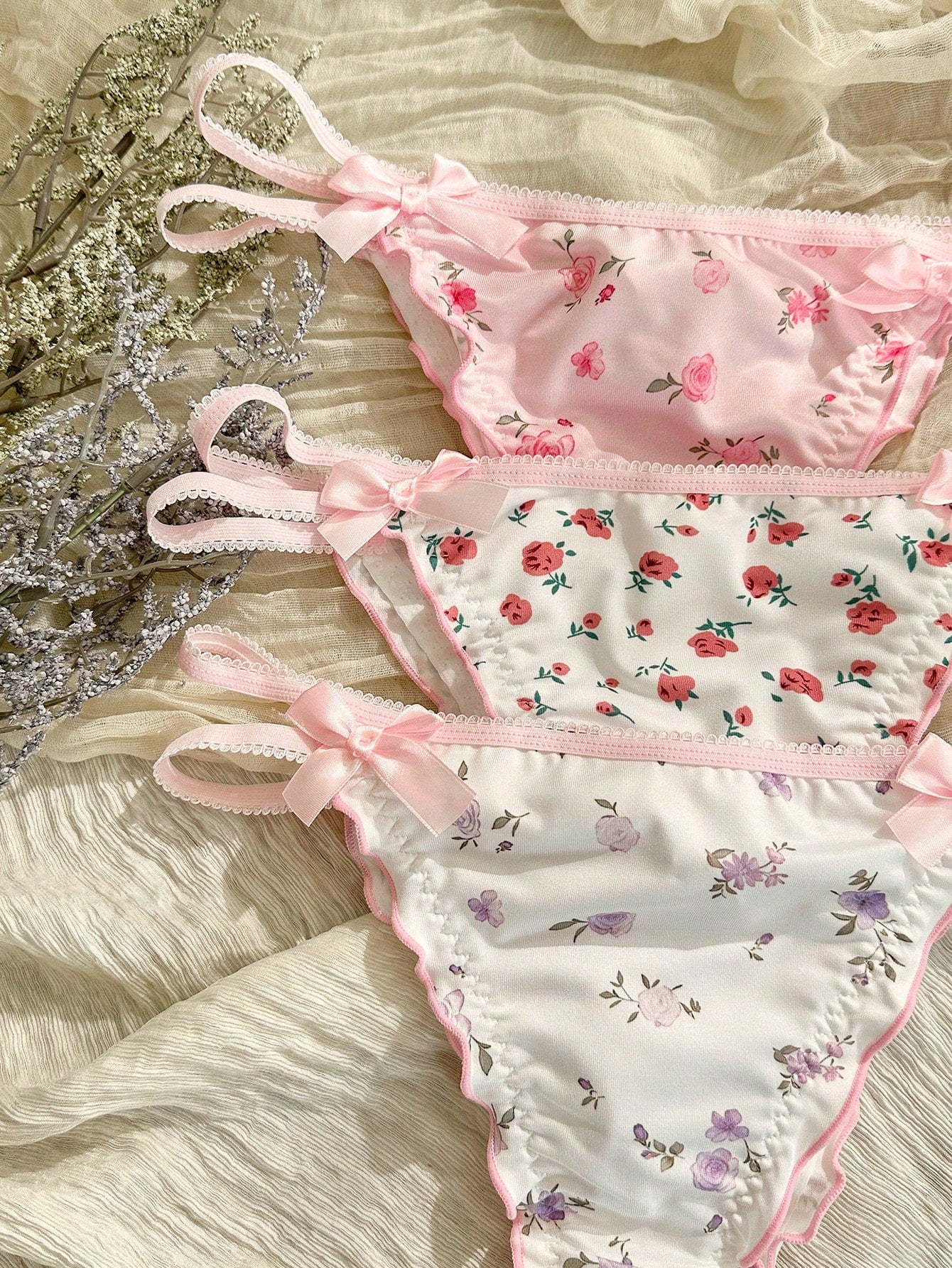 Three-piece set of pink women's low-rise brief panties with floral styling, bow waist accents, contrast lace, contrast binding, and cut-out details.