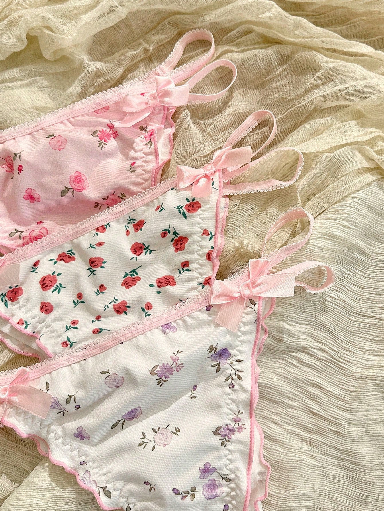 Three-piece set of pink women's low-rise brief panties with floral styling, bow waist accents, contrast lace, contrast binding, and cut-out details.