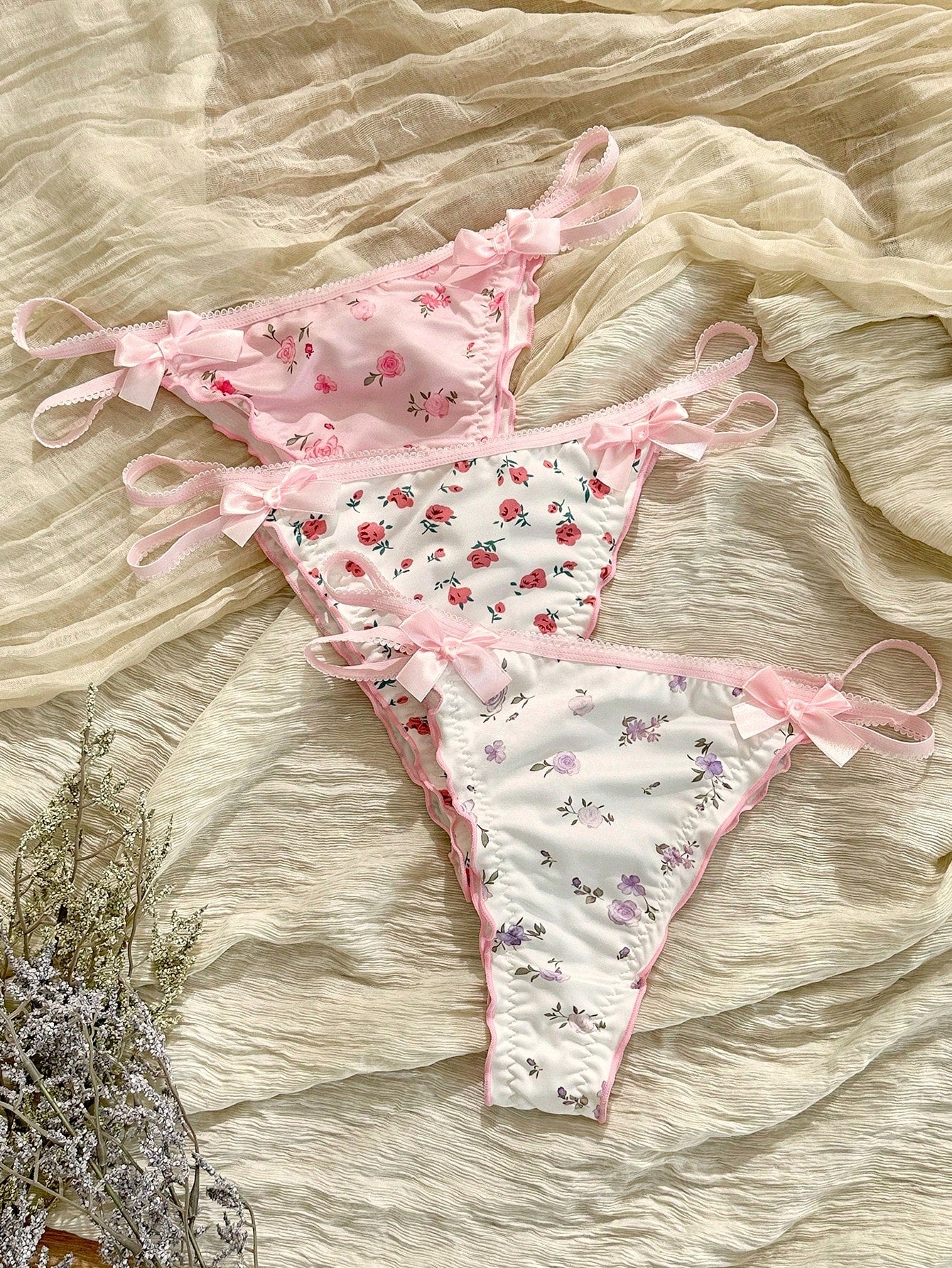 Three-piece set of pink women's low-rise brief panties with floral styling, bow waist accents, contrast lace, contrast binding, and cut-out details.