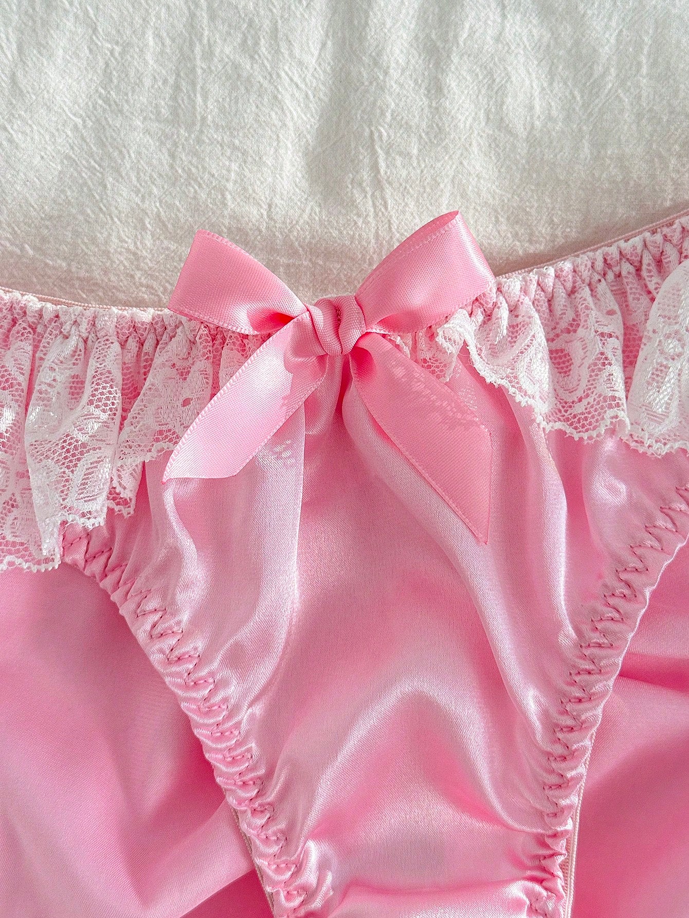 Women's pink low-rise triangle briefs with contrast lace, ruffle trim, bow detail, crisscross accents, and plant pattern