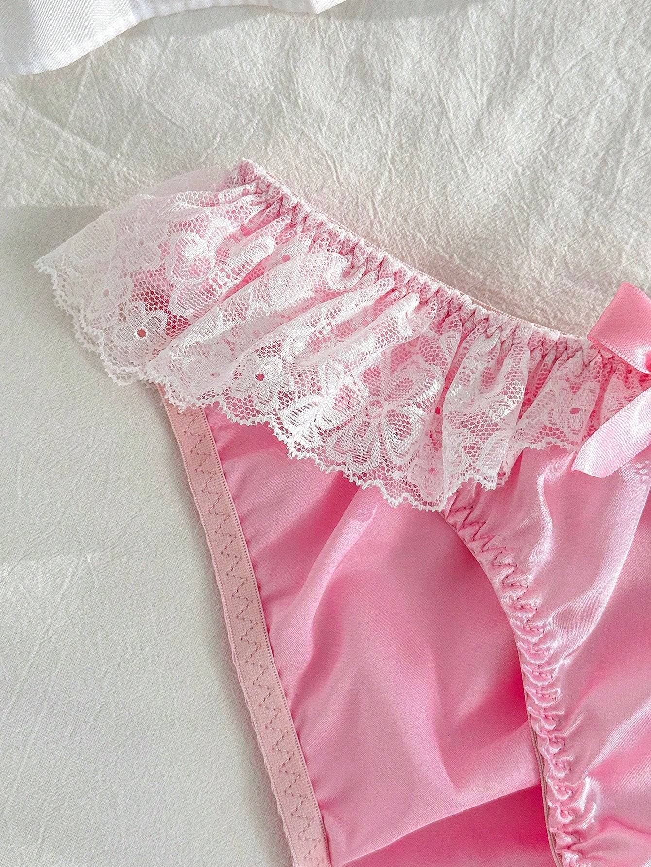 Women's pink low-rise triangle briefs with contrast lace, ruffle trim, bow detail, crisscross accents, and plant pattern