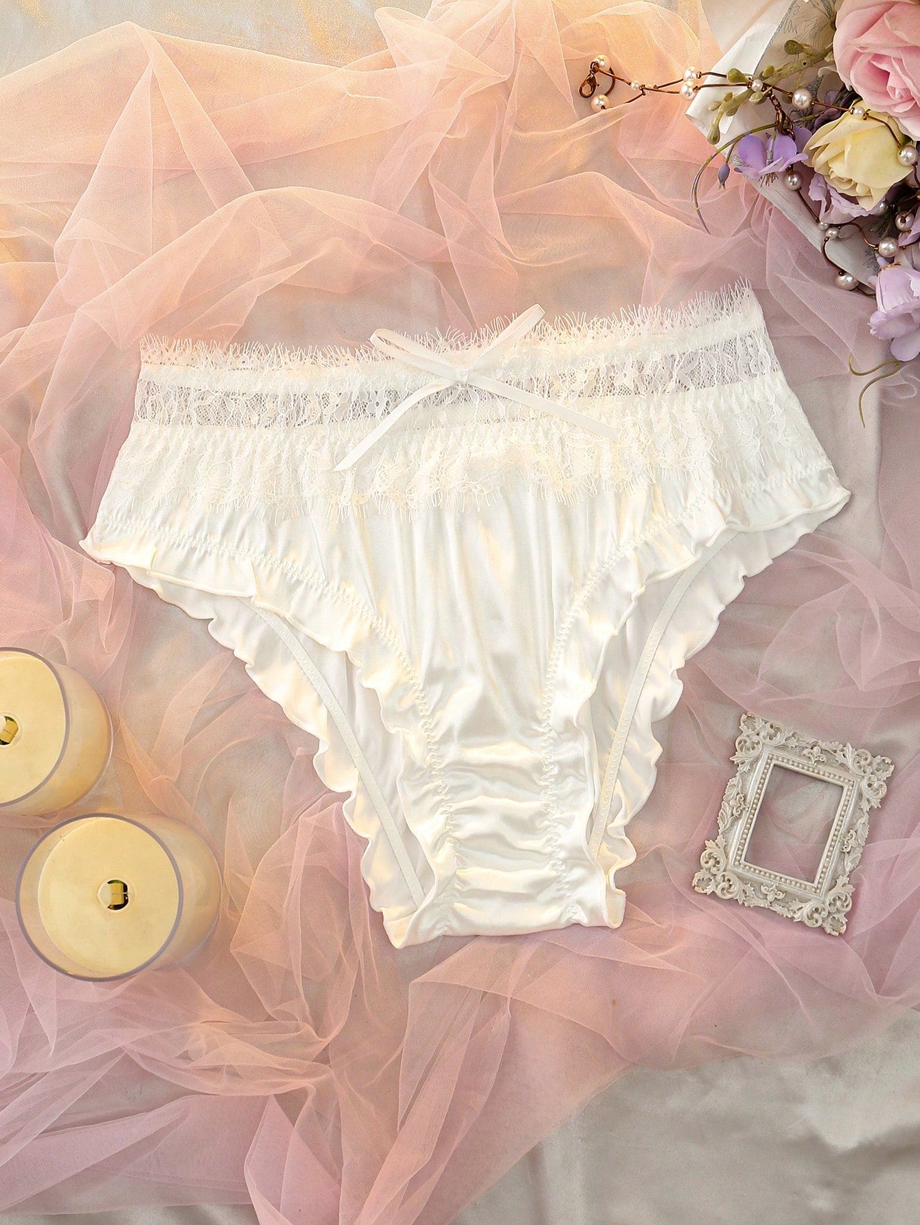 White satin-style low rise brief panties with contrast lace patchwork, bow detail, and lettuce trim